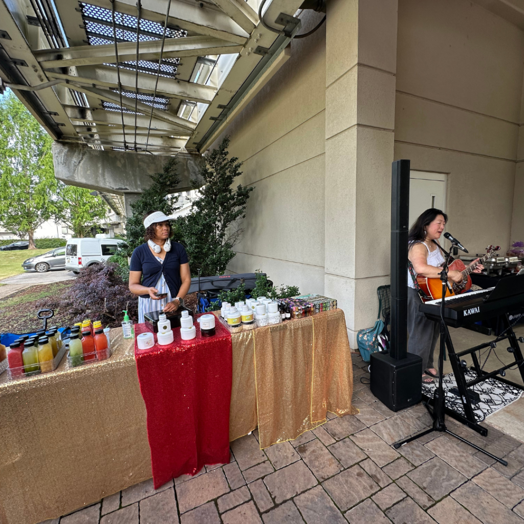 A vendor looks on as an entertainer sings into a microphone at a farmers market in downtown huntsville