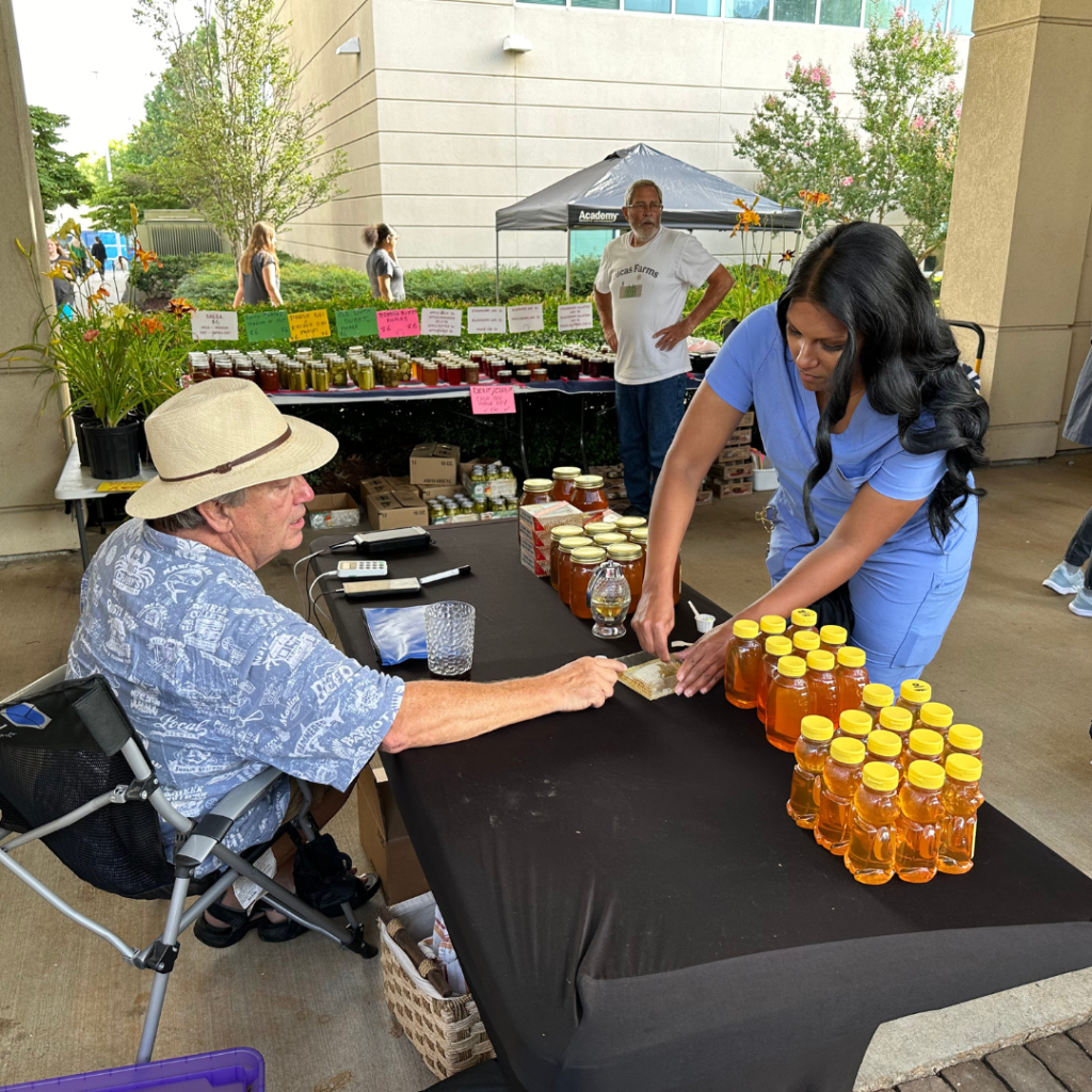 A woman in scrubs leans in to pay a vendor for honey at the huntsville farmers market